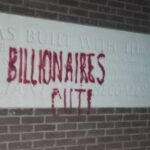 A picture of a wall with grafiti-ed on to it "Billionaires out!". The wall features a white stone that thanks the donators to this building, including the Thatcher familly.