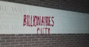 A picture of a wall with grafiti-ed on to it "Billionaires out!". The wall features a white stone that thanks the donators to this building, including the Thatcher familly.